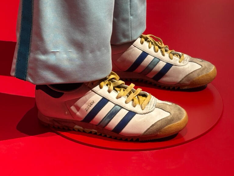 A pair of retro Adidas white leather sneakers with blue stripes and yellow laces.