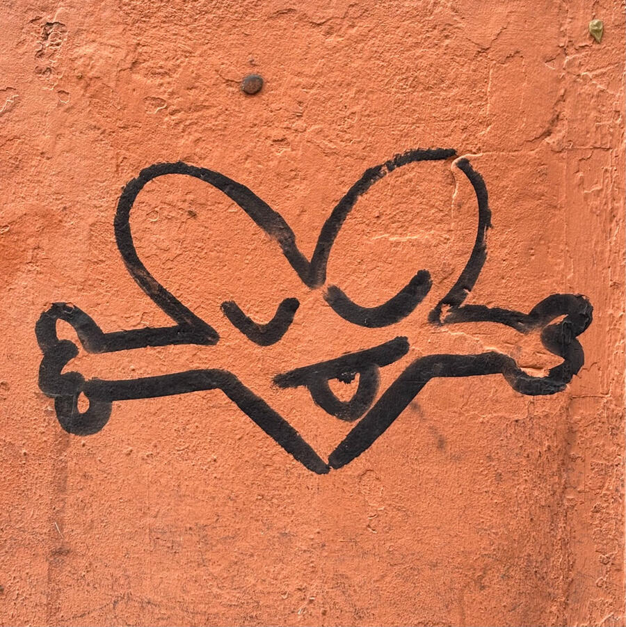 A simple black paint sketch on a faded red wall. A heart shape with arms and a face – the eyes are peacefully closed and the tongue is cheekily poking out.