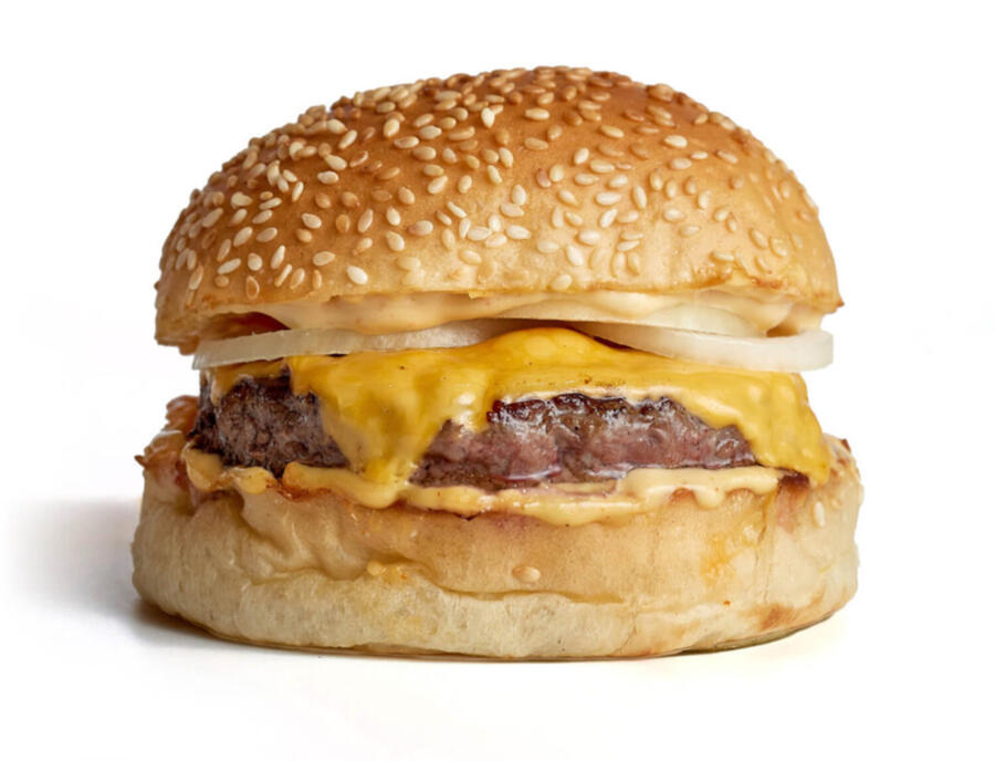 A studio photograph of a cheeseburger. It has a sesame seed bun, a single juicy beef patty, cheese melting down the edges, and visible rings of raw white onion.