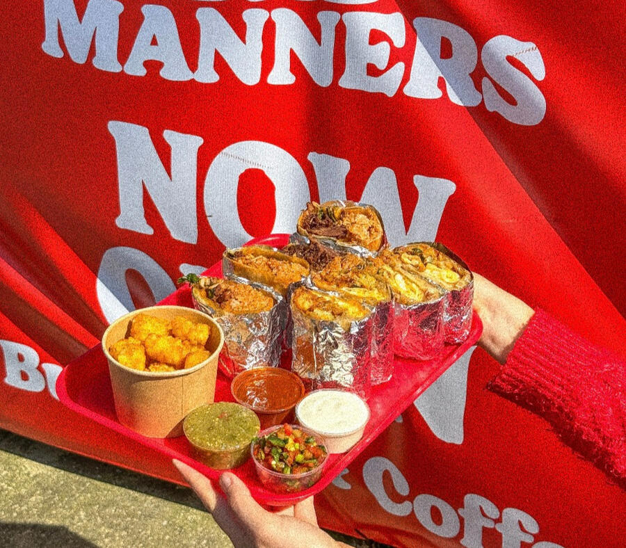 A hand holding a red plastic tray full of cut-in-half burritos, a pot of tater tots, and four pots of different salsas.
