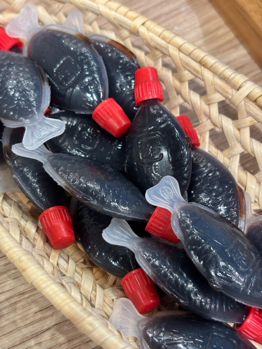 A close up of single-serve soy sauce containers. They are shaped like a fish, with a bright red screw-top cap.
