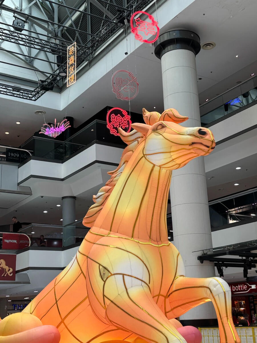 An upward view of a large orange inflatable horse. In the background, multiple floors of an indoor shopping centre are visible.
