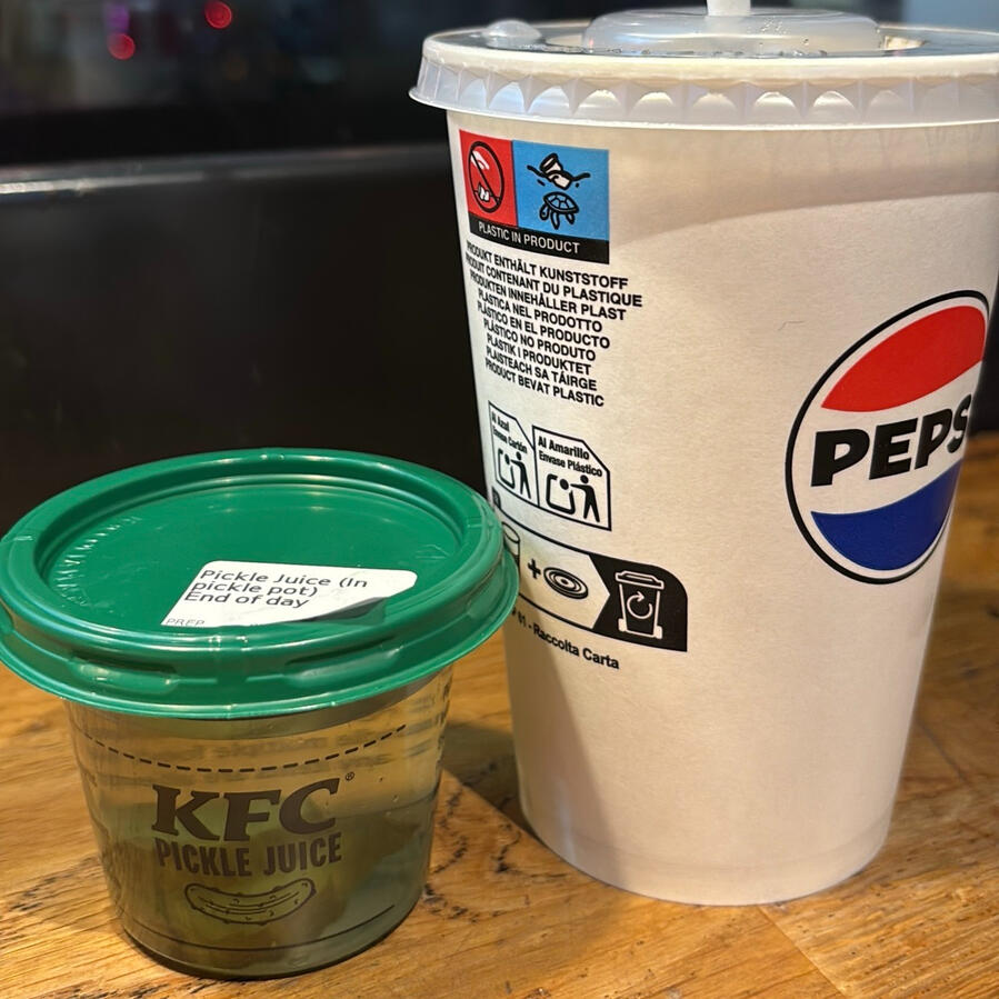 A plastic cup labelled "KFC pickle juice" sits next to a takeaway Pepsi cup.